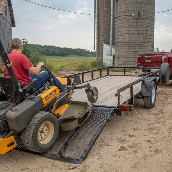 Lawn tractor driving up utility trailer ramps