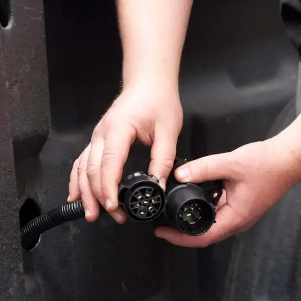 Two hands holding a CURT trailer plug and socket on the back of a pickup truck